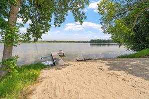 Um cenário à beira de um lago, com praia de areia, um píer e caiaques.
