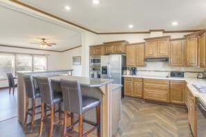 Une cuisine avec des meubles de rangement en bois, un îlot central doté de tabourets, un réfrigérateur et un four à micro-ondes.