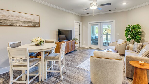 A modern living room with a dining area, a ceiling fan, and a large window. - Family Getaway in Calabash w/ Pool; 9 Mi to Beach (Calabash)