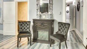 Una habitación con chimenea, dos sillones tapizados, un espejo con marco decorativo y una puerta que da a otra estancia.