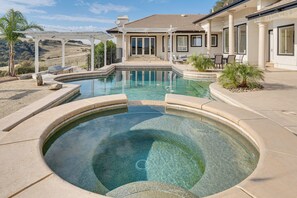 Una piscina con hidromasaje, un patio cubierto y vistas a las colinas.