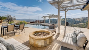 Ein Poolbereich mit Feuerstelle, Gartenmöbeln und einer Pergola mit Blick auf eine malerische Landschaft.