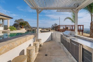 Cocina exterior con parrilla, zona de estar y piscina.