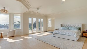 Ein geräumiges Schlafzimmer mit einem großen Bett, einem modernen Sessel und Blick durch Glastüren.