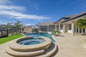 A swimming pool with a hot tub, surrounded by a landscaped yard with palm trees and a view of a mountain range.