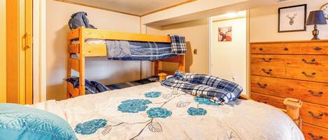 Una cama individual con colcha estampada y almohada azul, cómoda de madera y un cuadro de un venado enmarcado en la pared.