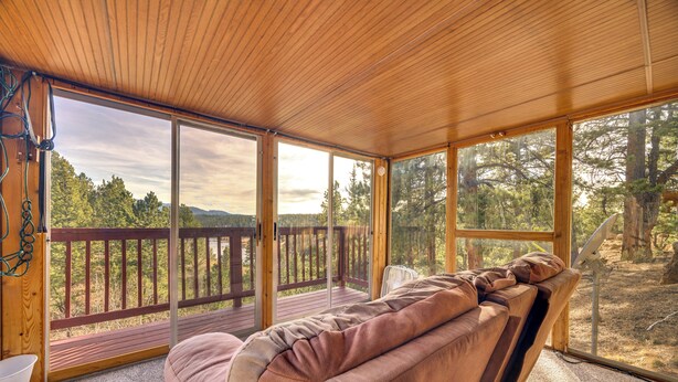 A cozy cabin with a large sliding glass door leading to a deck, a cushioned bench, and a view of a forested landscape. - Close to Pike Natl Forest! Lake-view Family Cabin (Divide)