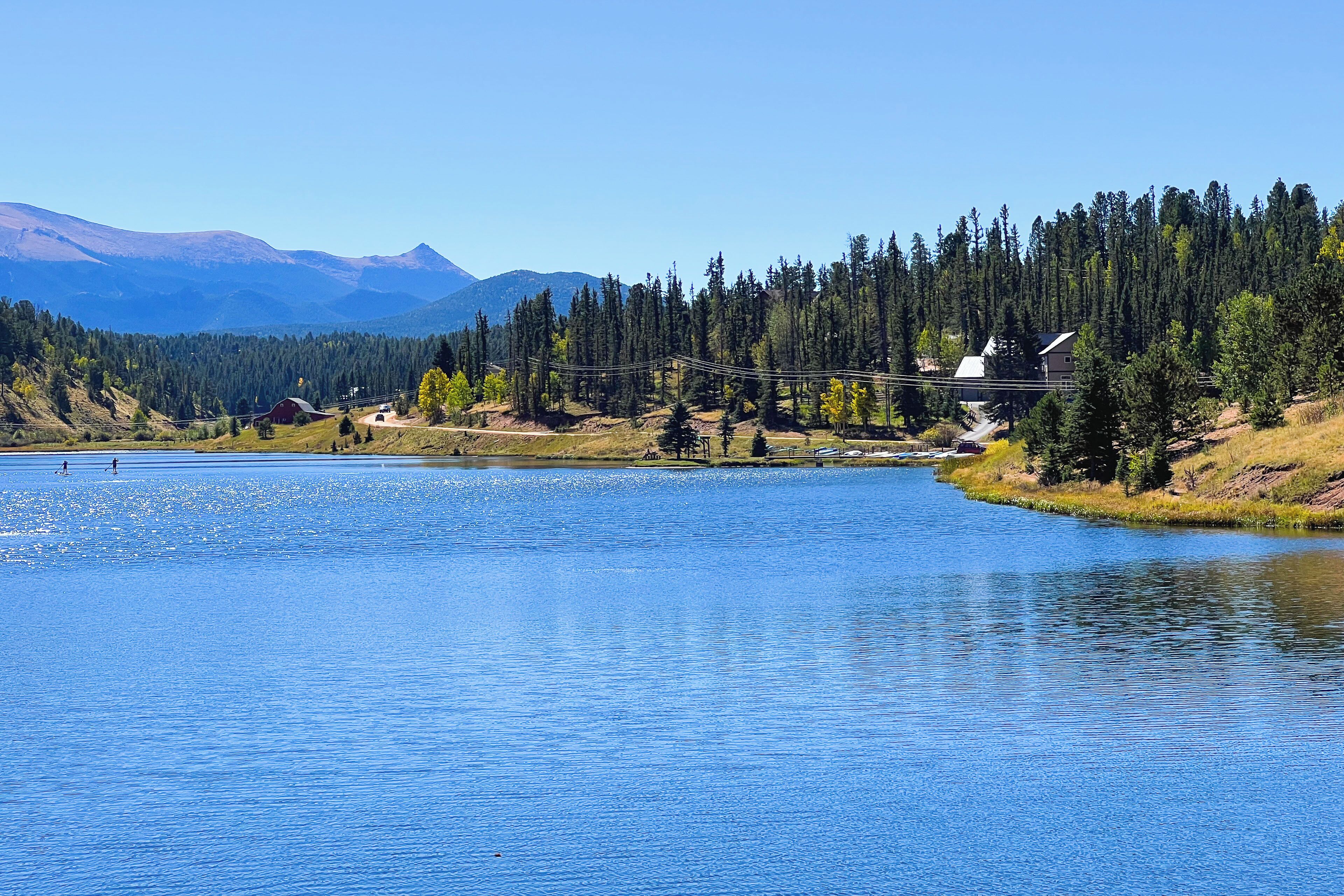 Une vue paisible sur un lac, avec une maison et des montagnes boisées en arrière-plan.