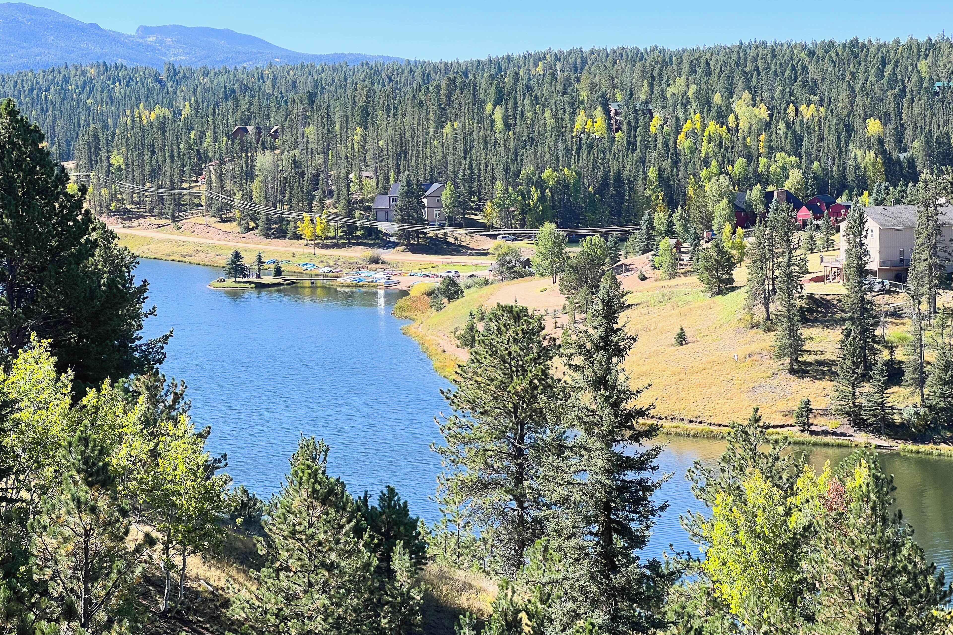 Une vue sur un lac, avec une zone boisée, un petit quai et des bâtiments en arrière-plan.