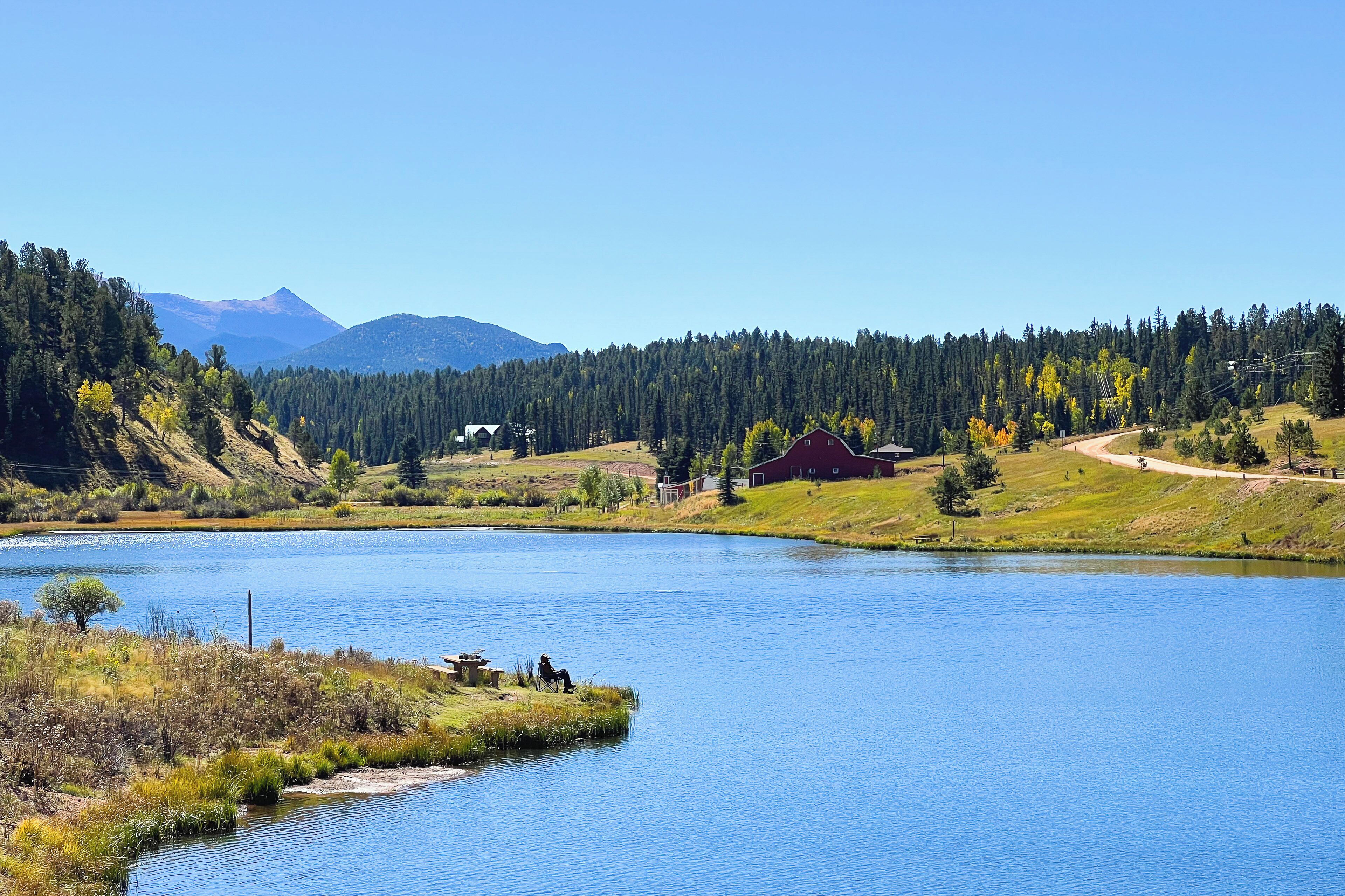 Un lago rodeado de colinas boscosas y un granero rojo.
