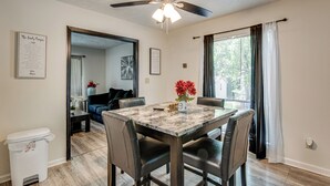 Uma área de refeições com mesa, cadeiras, um ventilador de teto e vista para o exterior através de uma janela.