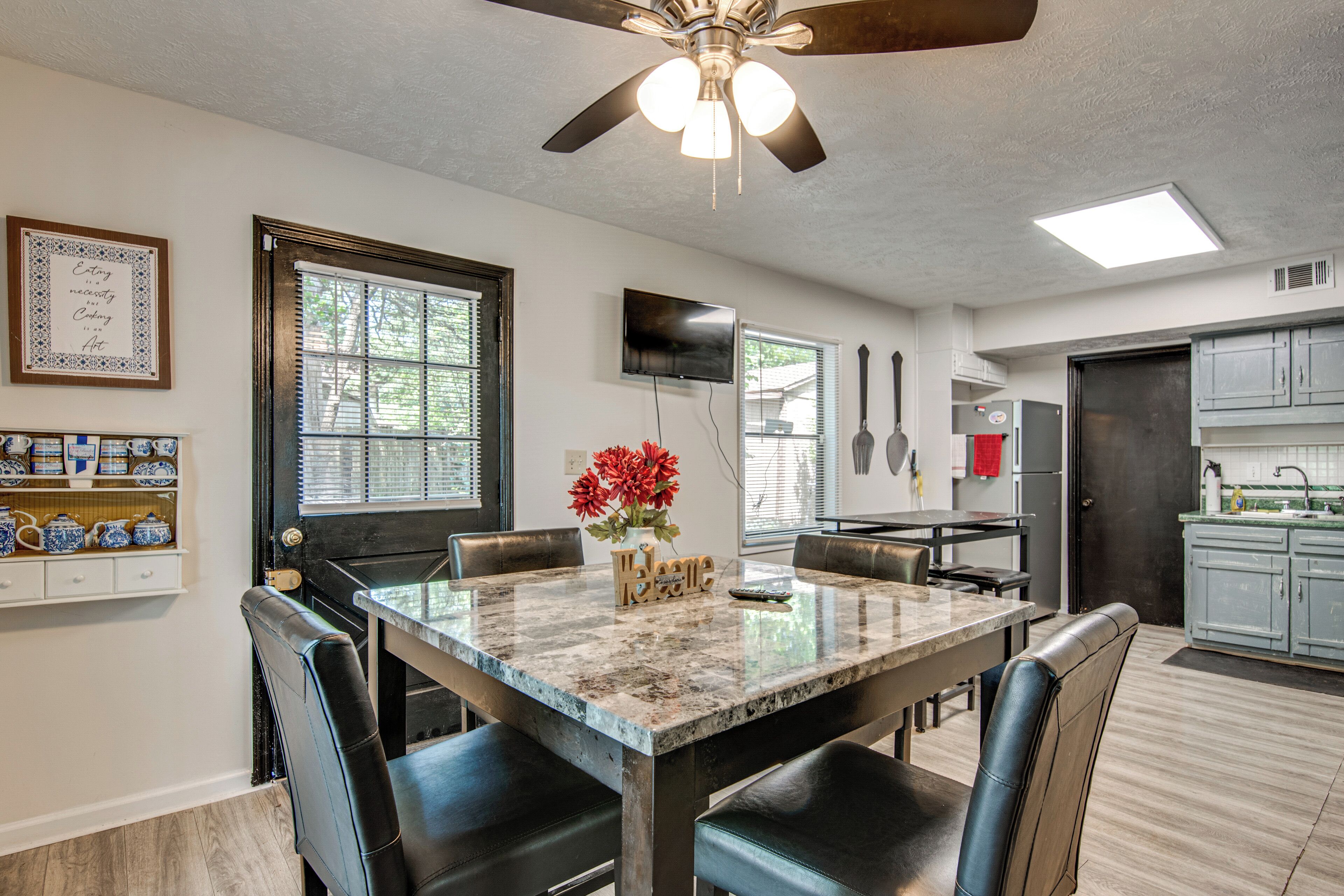A dining area with a table, chairs, a ceiling fan, and a kitchen in the background.