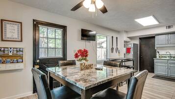 A dining area with a table, chairs, a ceiling fan, and a kitchen in the background.