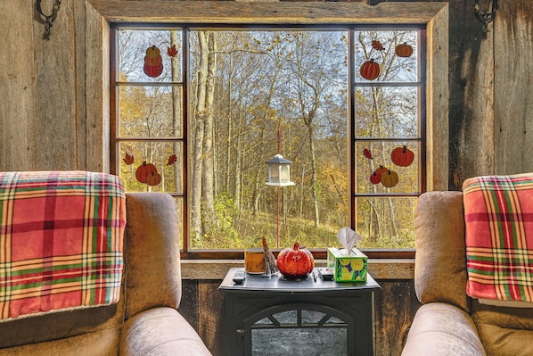 A cozy room with a large window, a small table with a lantern, and plaid cushions. - 9 Mi to Hocking Hills SP: Cabin w/ Private Hot Tub (Lancaster)