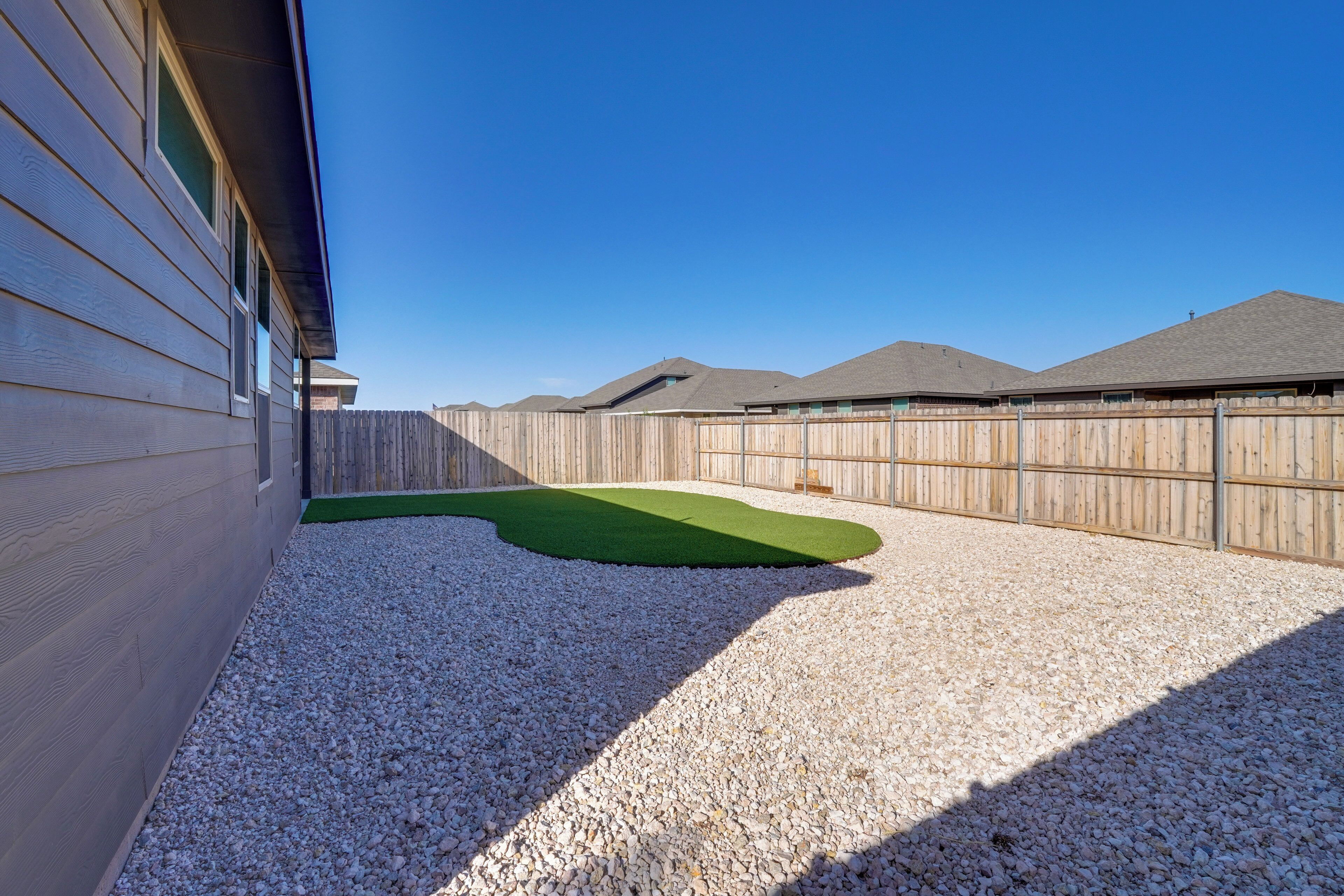 A backyard with a wooden fence, a gravel surface, and a green artificial turf area.