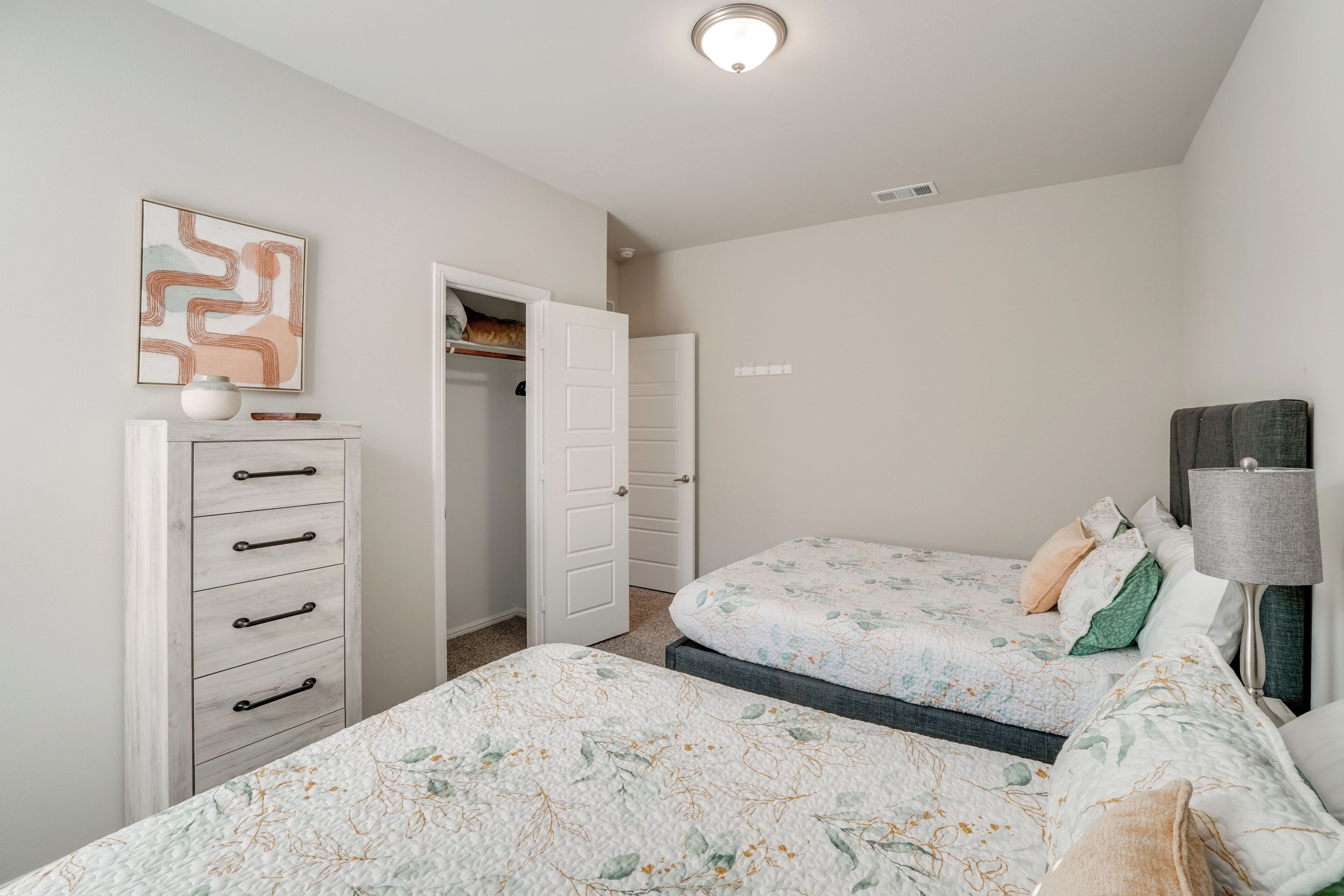 A bedroom with two beds, a dresser, a door, and a lamp.