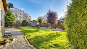 Un patio trasero residencial con césped cuidado, un sendero de grava y varios arbustos y árboles.