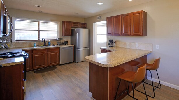 A kitchen with wooden cabinets, a stainless steel refrigerator, a granite countertop, and two bar stools. - 1 Mi to Enmu: Portales Family Home w/ Yard! (Portales)
