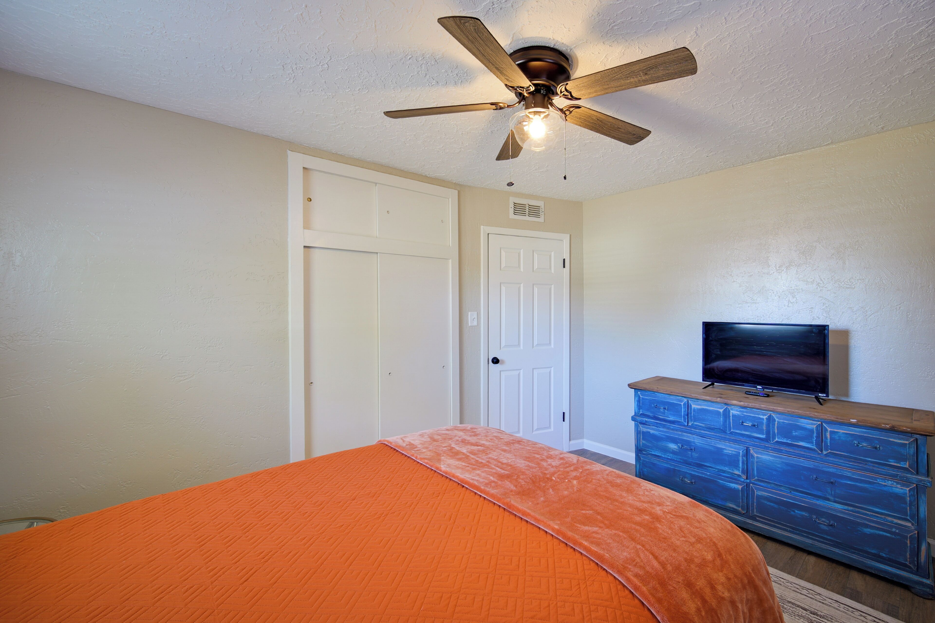A bedroom with a bed, a ceiling fan, a dresser, and a television.