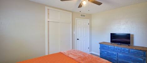A bedroom with a bed, a ceiling fan, a dresser, and a television.