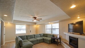 A living room with a sectional sofa, a ceiling fan, a fireplace, and a television on the wall. - 1 Mi to Enmu: Portales Family Home w/ Yard! (Portales)