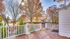 A wooden deck with a white railing, surrounded by trees with autumn leaves, and a white building in the background. - Quiet Home Base in the Heart of Boardman! (Boardman)