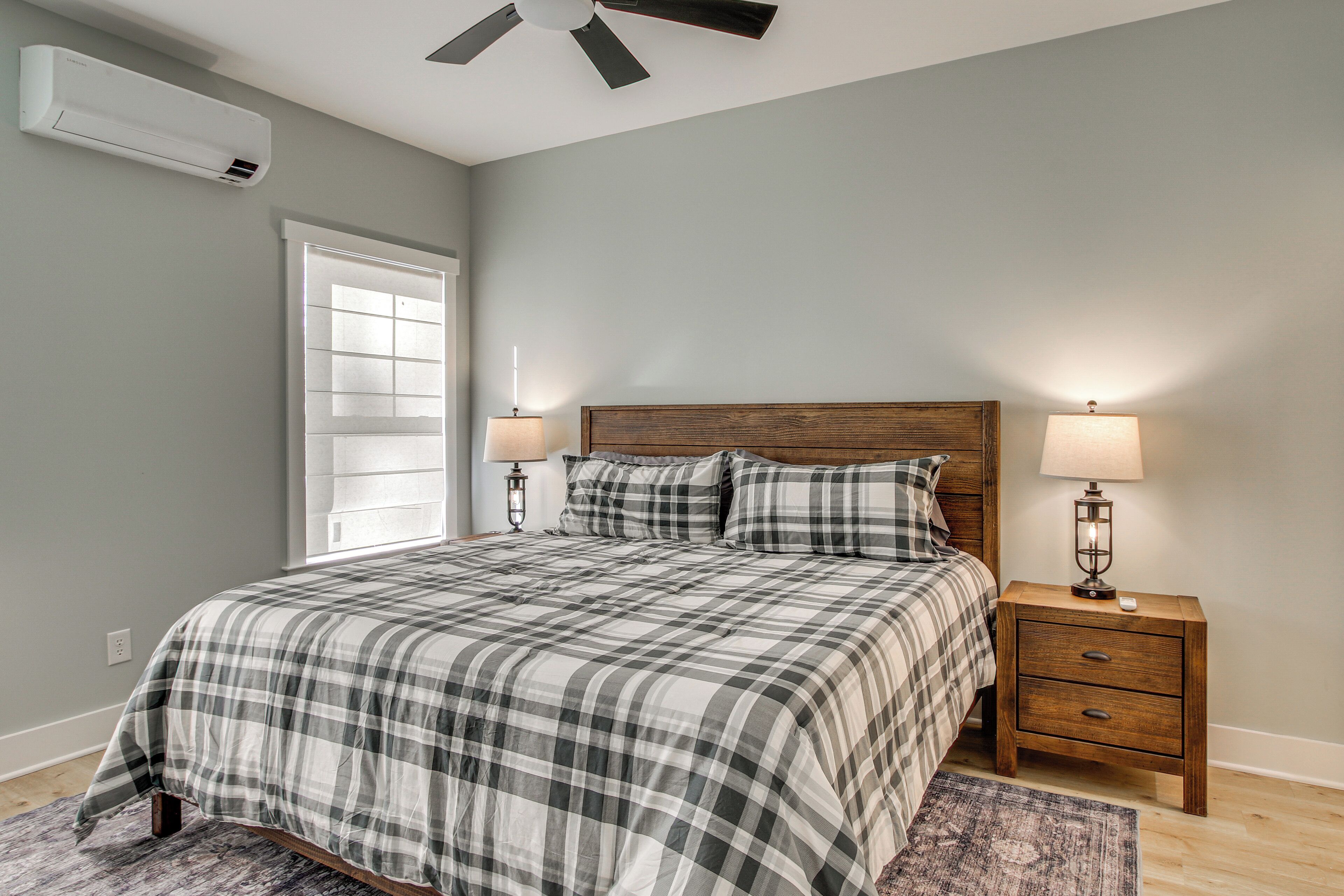 A bedroom with a bed, two bedside tables with lamps, a ceiling fan, and an air conditioning unit.