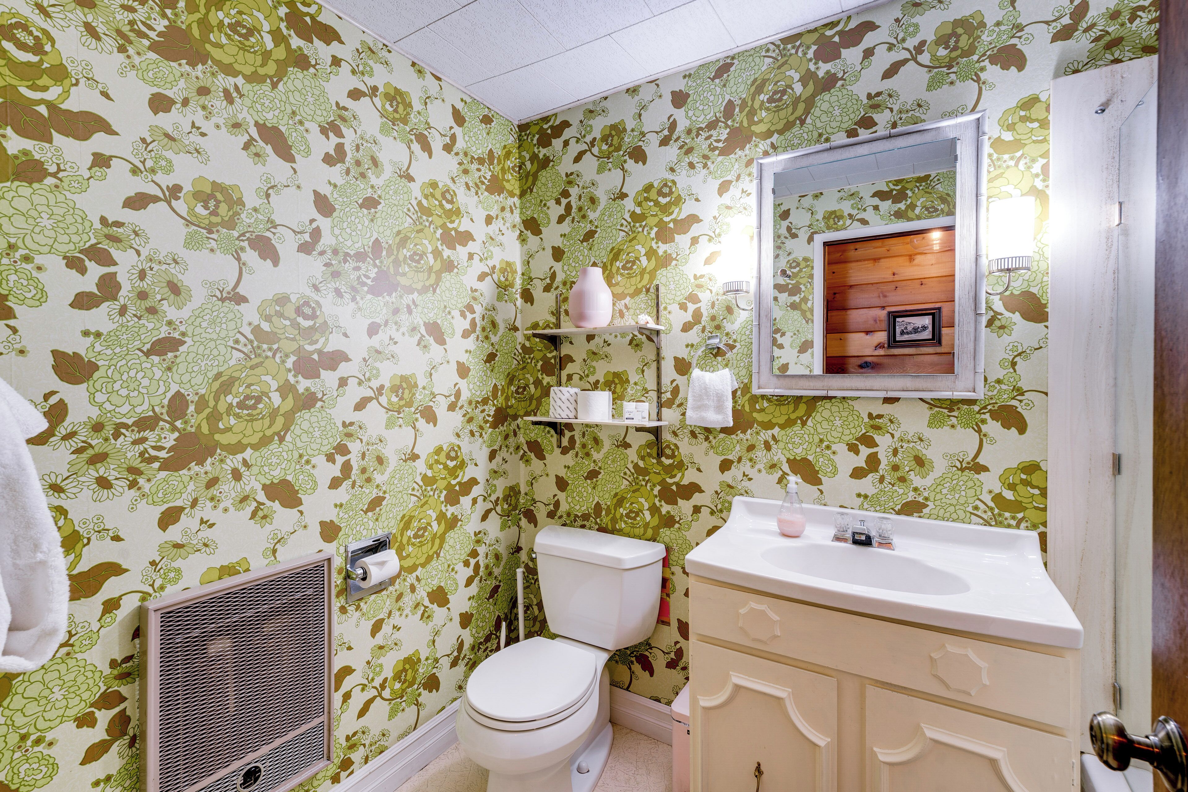A bathroom with floral wallpaper, a toilet, a sink, and a mirror.