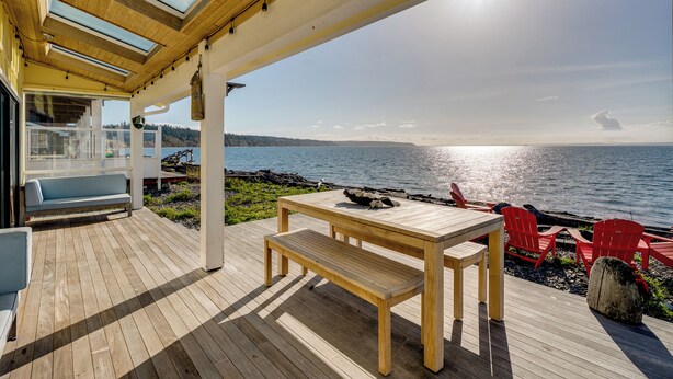 Eine Holzterrasse mit Tisch und Bänken, die auf ein Gewässer blickt.