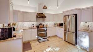 A modern kitchen with white cabinets, stainless steel appliances, and pendant lighting.