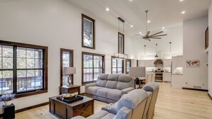 A spacious living area with a sofa, a coffee table, and a dining table. There are large windows providing natural light and a view of the outdoors.