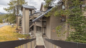 A multi-story building with a central staircase, outdoor seating area, and a view of the surrounding landscape. - Beautiful Mountain Views, walking distance to Big Sky Resort! (Big Sky)
