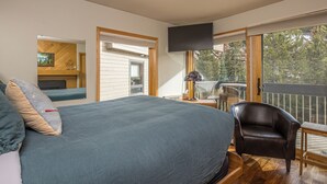 A bedroom with a large bed, a chair, a TV, and a balcony with a view of trees. - Beautiful Mountain Views, walking distance to Big Sky Resort! (Big Sky)