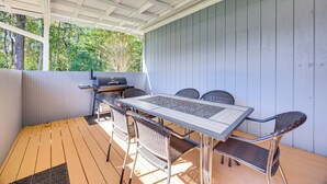 Um pátio externo com mesa, cadeiras, churrasqueira e vista para árvores.