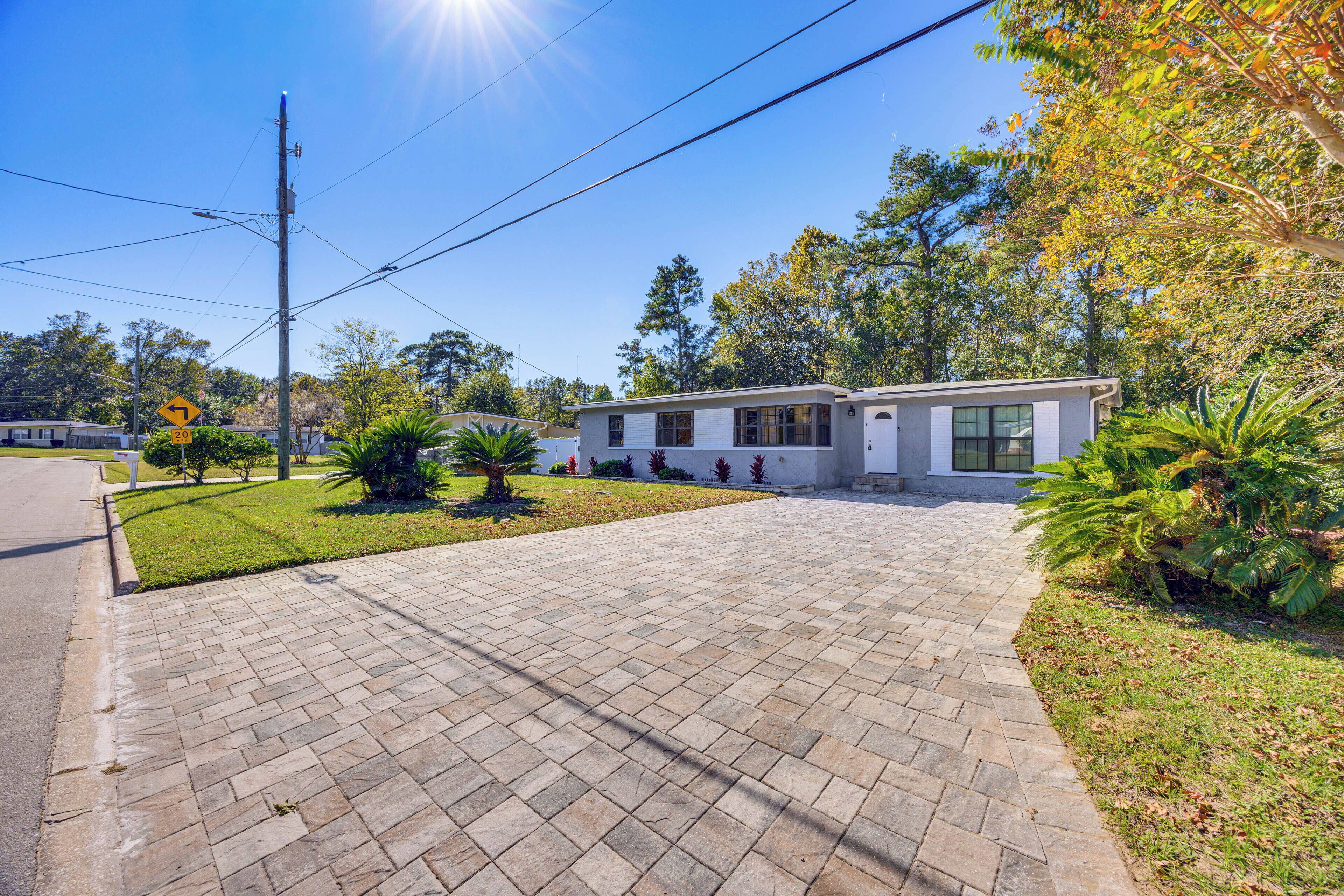 A modern single-story house with a paved driveway, surrounded by well-maintained landscaping and trees.