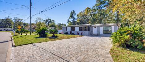 A modern single-story house with a paved driveway, surrounded by well-maintained landscaping and trees.