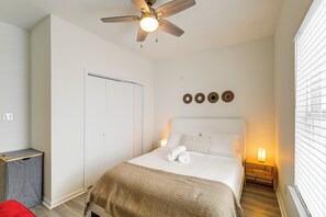 A bedroom with a bed, a ceiling fan, a bedside table with a lamp, a wardrobe, and a window with blinds. - Modern Home I Near NRG I Easy Light Rail Access (Houston)