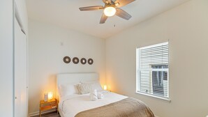 A bedroom with a bed, bedside lamps, a ceiling fan, a window with blinds, and wall decor. - Modern Home I Near NRG I Easy Light Rail Access (Houston)