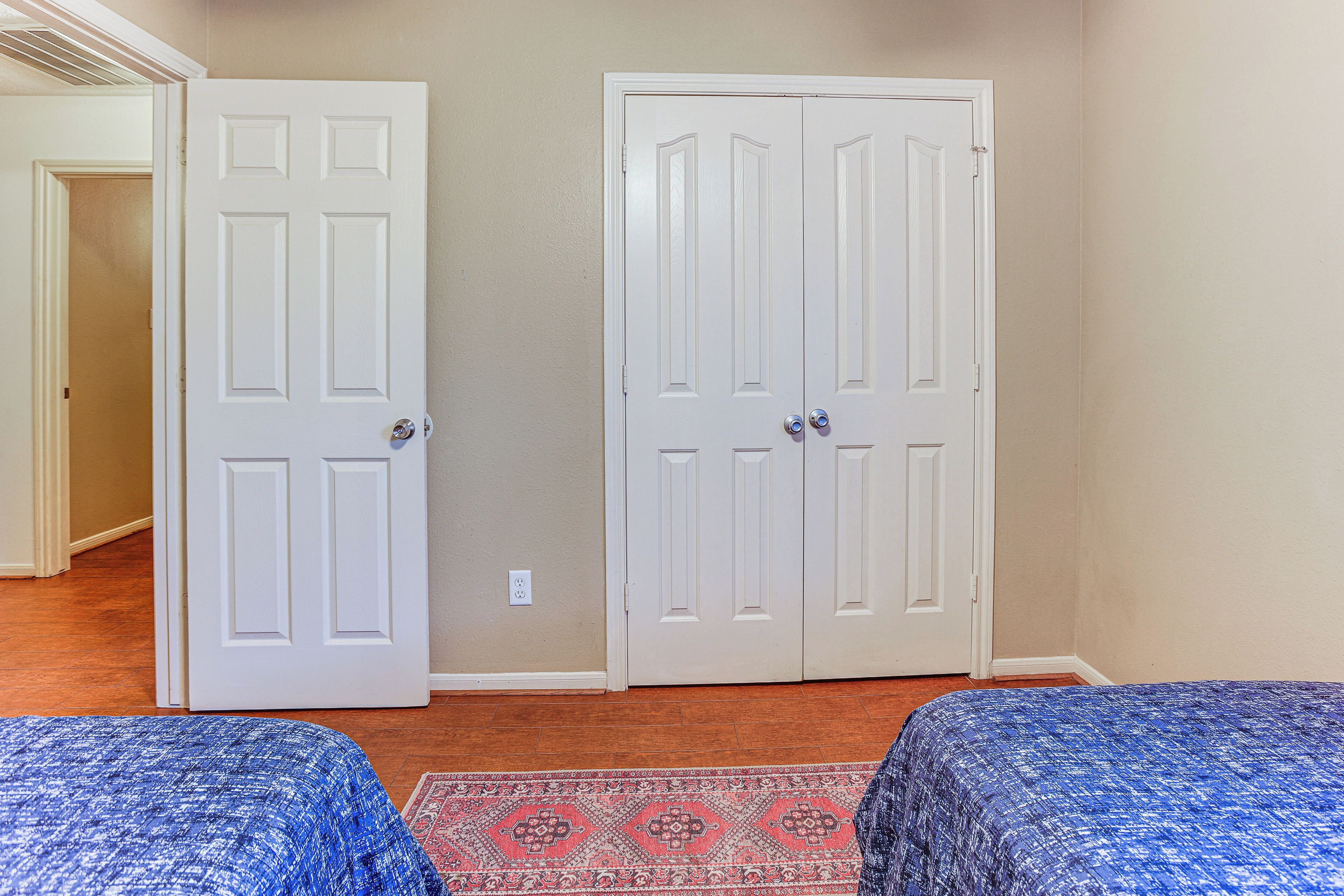 A bedroom with two beds, a patterned rug, and two white doors.
