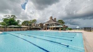 Una piscina con varias pistas de natación, un área de estar techada y un edificio con una chimenea al fondo.