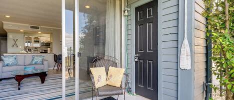 A sliding glass door leading to a living room with a sofa, a coffee table, and a chair with cushions.