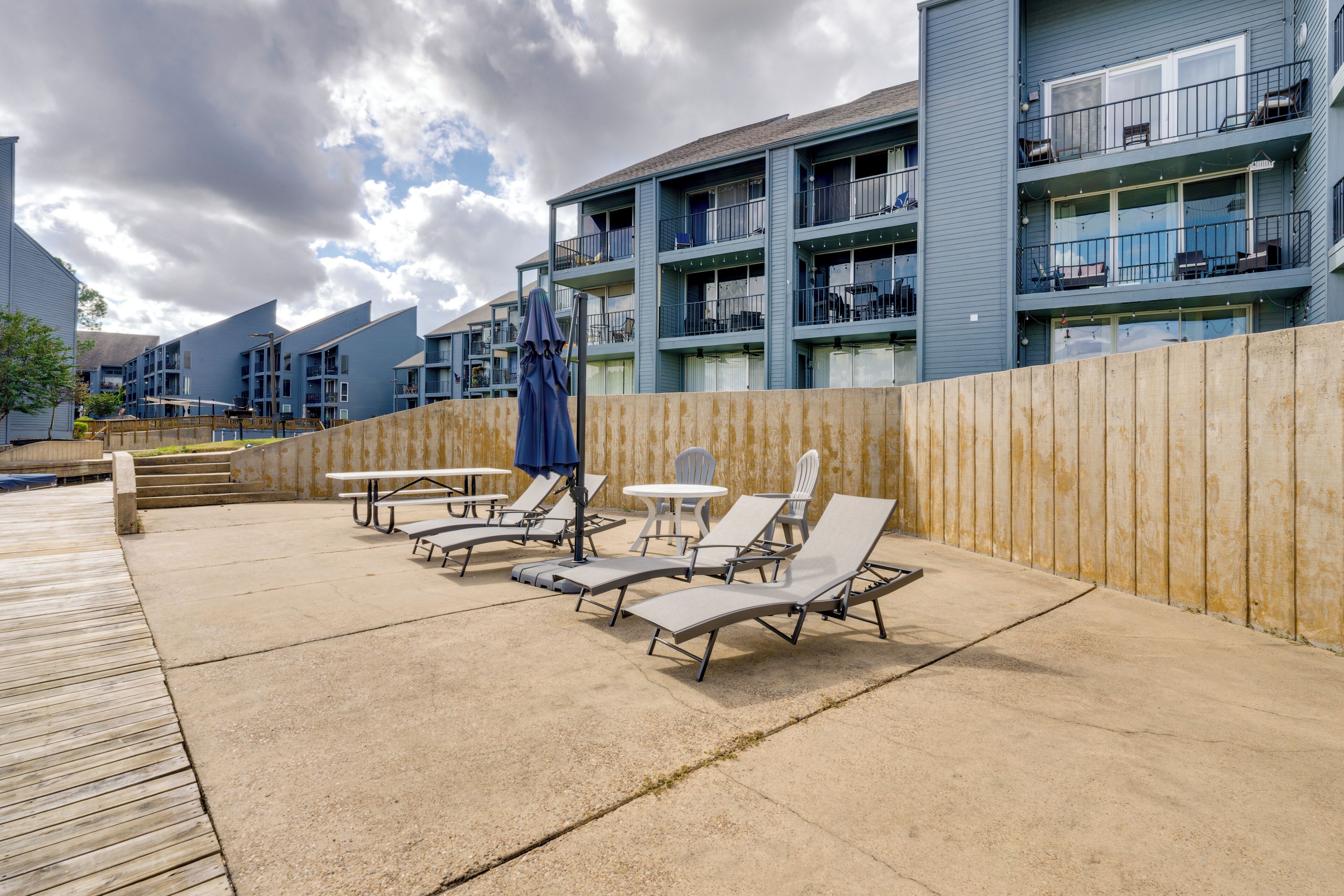 A resort with a pool area featuring lounge chairs and tables, a wooden deck, and a backdrop of multi-story buildings with balconies.