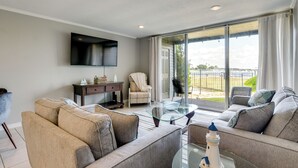 Una sala de estar moderna con un sofá, una mesa de centro de vidrio, un televisor montado en la pared y vistas a través de grandes puertas corredizas de vidrio.