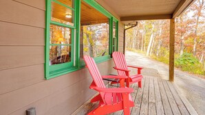 A wooden porch with two red Adirondack chairs and a table, overlooking a forested area. - Hike On-site! 16-acre Escape Near Shenandoah NP (Stanley)