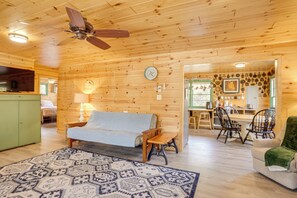 A cozy log cabin interior with a sofa, dining table, chairs, and a ceiling fan.