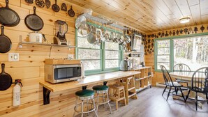 A wooden interior with a kitchen area featuring a microwave, stove, and various cookware. There are wooden stools and a dining table with chairs. - Hike On-site! 16-acre Escape Near Shenandoah NP (Stanley)