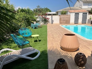 A backyard with a swimming pool, a white lounge chair, a blue chair, and a small table.