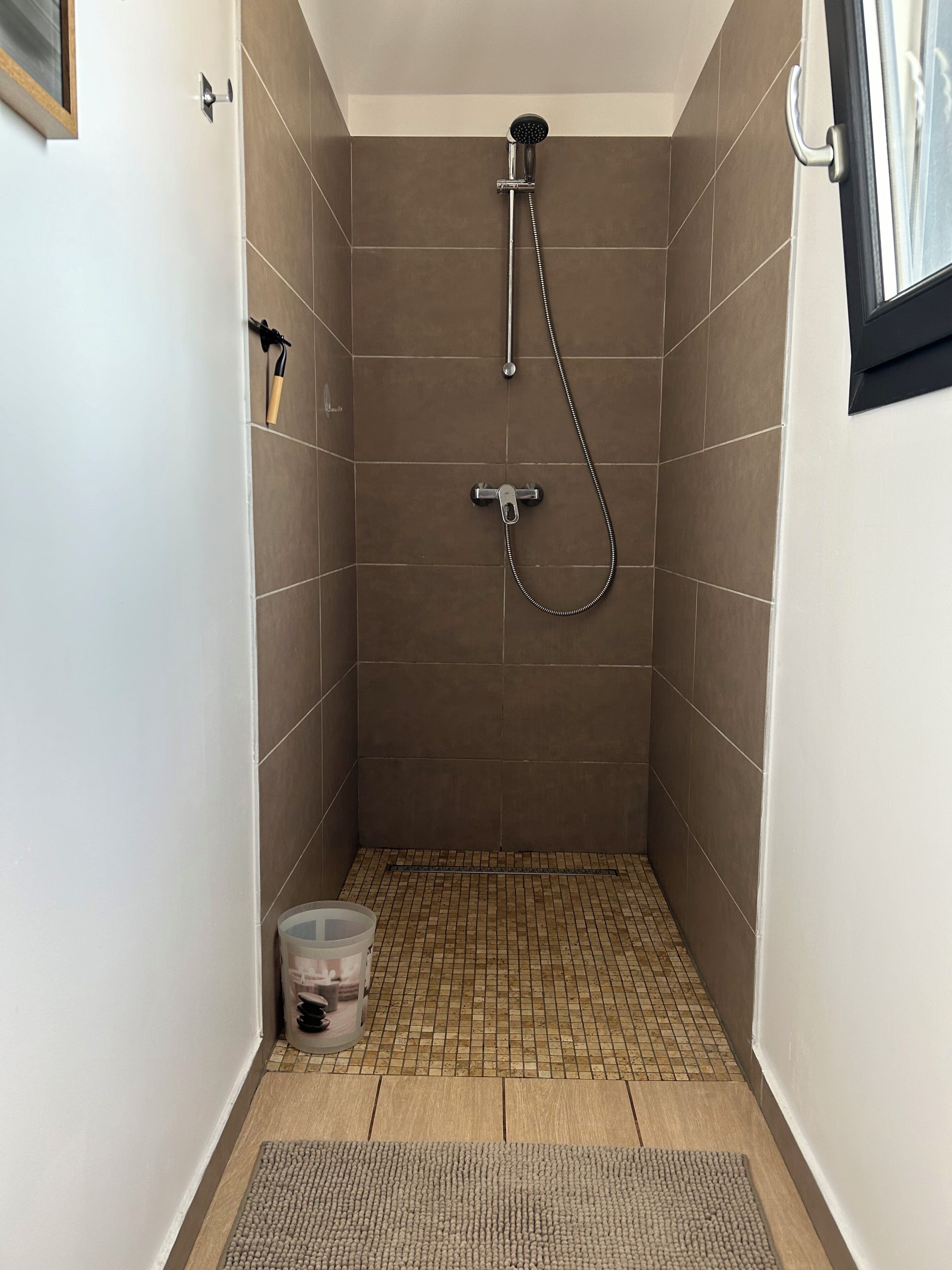 Un baño pequeño con azulejos, ducha de mano y grifo instalado en la pared.