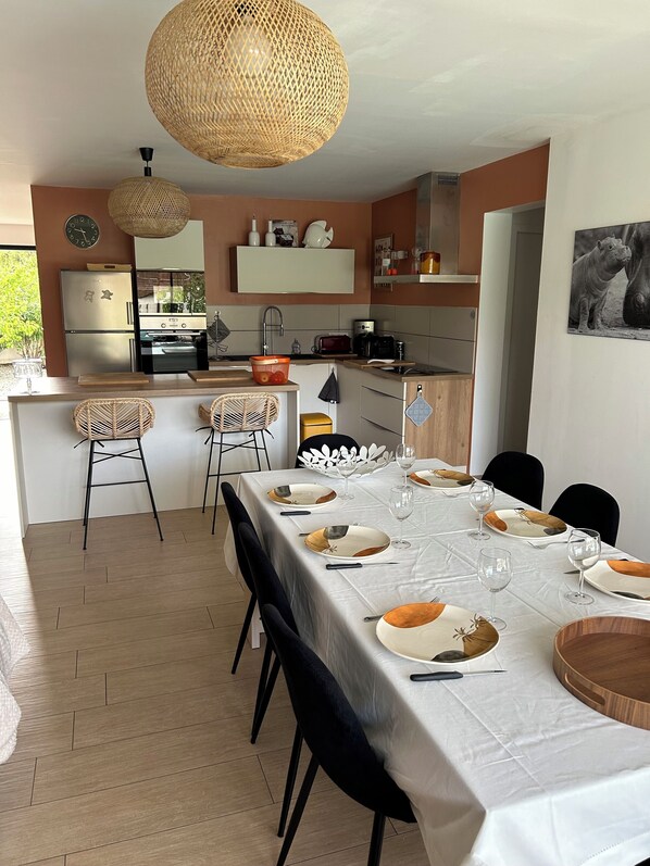 Une cuisine moderne avec un îlot central, un coin repas avec une nappe blanche et un luminaire suspendu en fibres tressées.