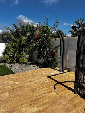 Une terrasse en bois avec une porte en métal, entourée de verdure et sous un ciel dégagé.